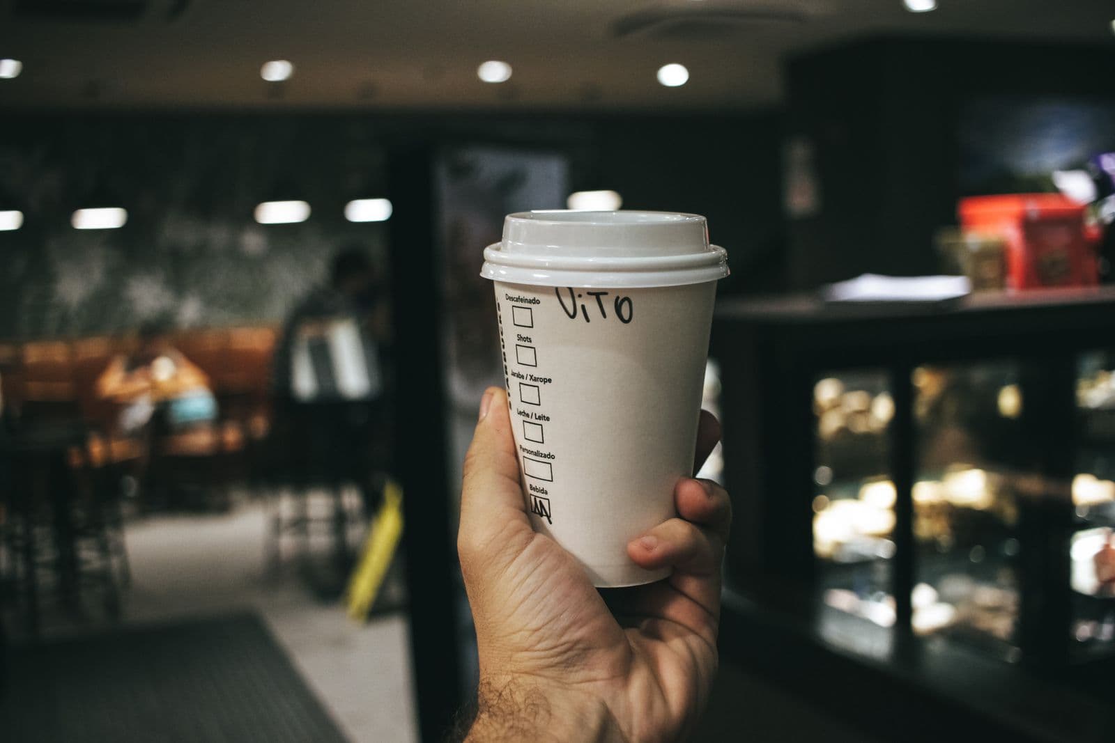 A takeaway coffee cup with a customer name handwritten in marker